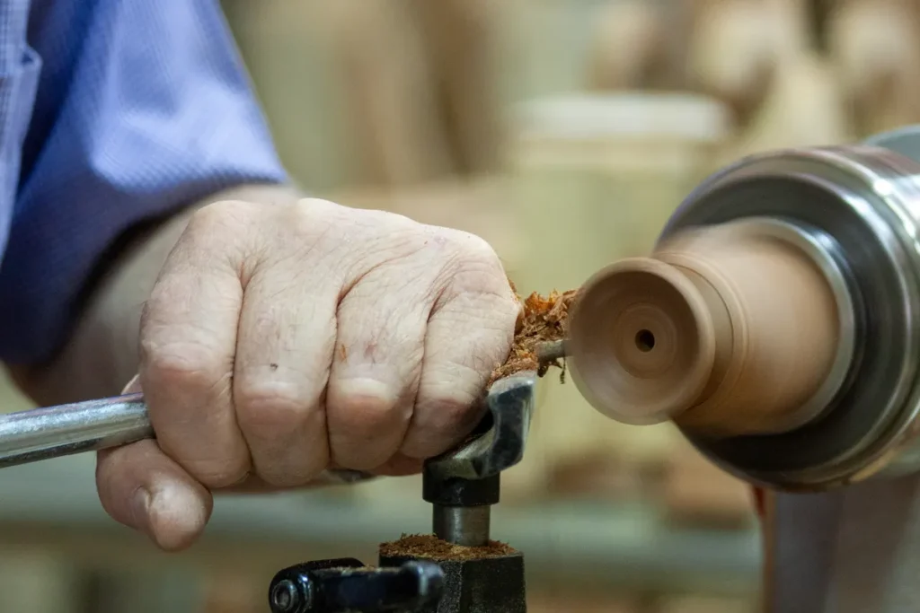 Close-up of craftsman's hand shaping wood on a lathe, showcasing precision and skill