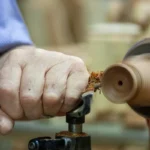 Close-up of craftsman's hand shaping wood on a lathe, showcasing precision and skill