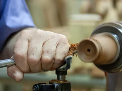 Close-up of craftsman's hand shaping wood on a lathe, showcasing precision and skill
